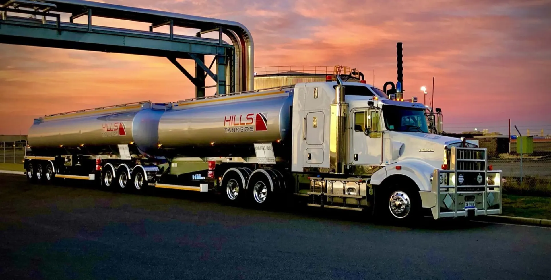 Hills Tankers Kenworth prime mover with a double tanker trailer at a fuel terminal under a sunset sky