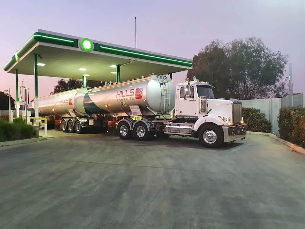 Hills Tankers fuel tanker delivering under a service station canopy at dusk