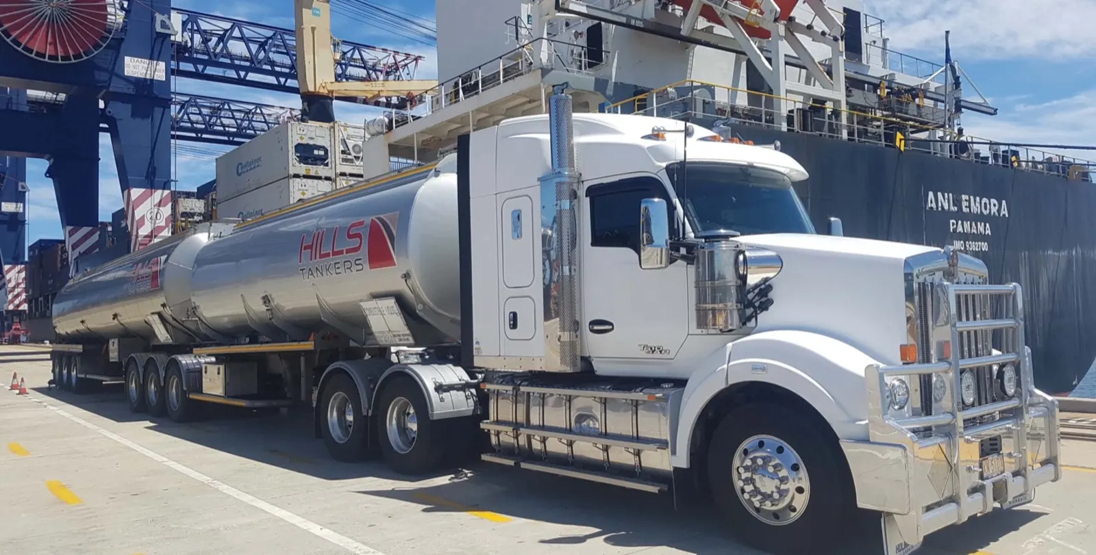 Hills Tankers semi at a shipping port beside a cargo vessel