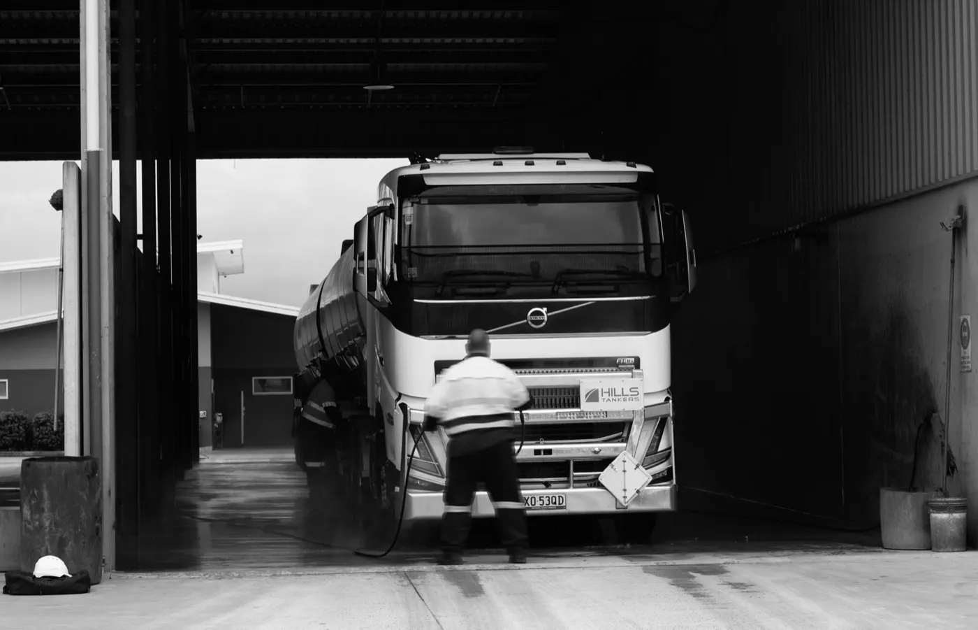 Wash bay attendant pressure-washing the front of a Volvo tanker at Hills Truck Wash